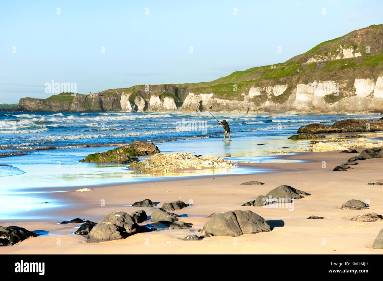 Les Roches Blanches également appelé East Strand à Portrush. Le Château de Dunluce à distance. L'homme pêche en mer. Le comté d'Antrim en Irlande du Nord Banque D'Images