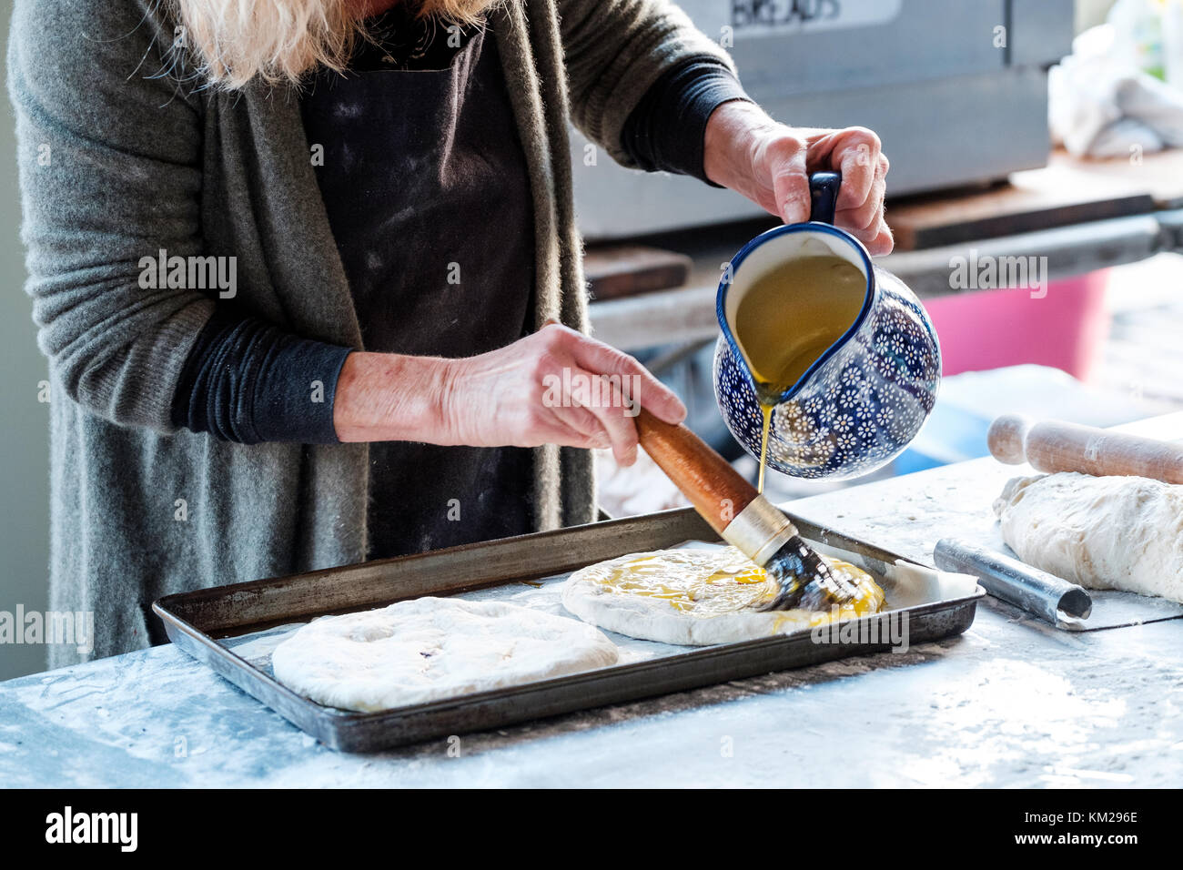 Une femelle baker prépare focaccia pain plat italien à un décrochage de plein air il est jeter de l'huile sur le dessus de la pâte avant il est placé dans un four à cuire Banque D'Images