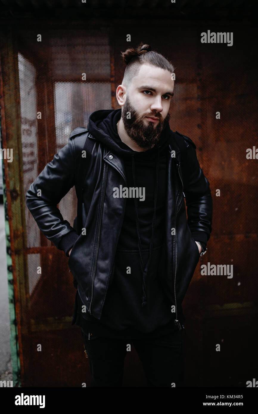 Jeune homme barbu moderne en noir vêtements de style l'article en contexte urbain. Banque D'Images Jeune homme barbu moderne en noir vêtements de style l'article en contexte urbain. Banque D'Images