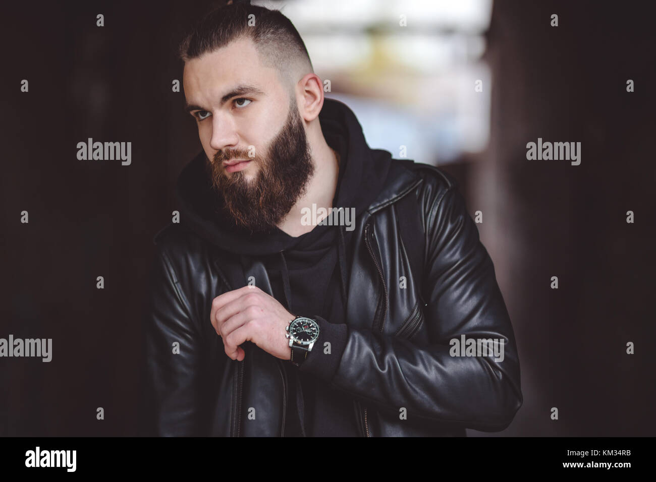 Jeune homme barbu moderne en noir vêtements de style l'article en contexte urbain. Banque D'Images Jeune homme barbu moderne en noir vêtements de style l'article en contexte urbain. Banque D'Images