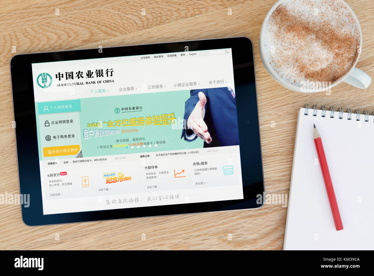 La banque agricole de Chine Site sur un iPad tablet device qui repose sur une table en bois à côté d'un bloc-notes et un crayon et une tasse de café. Banque D'Images