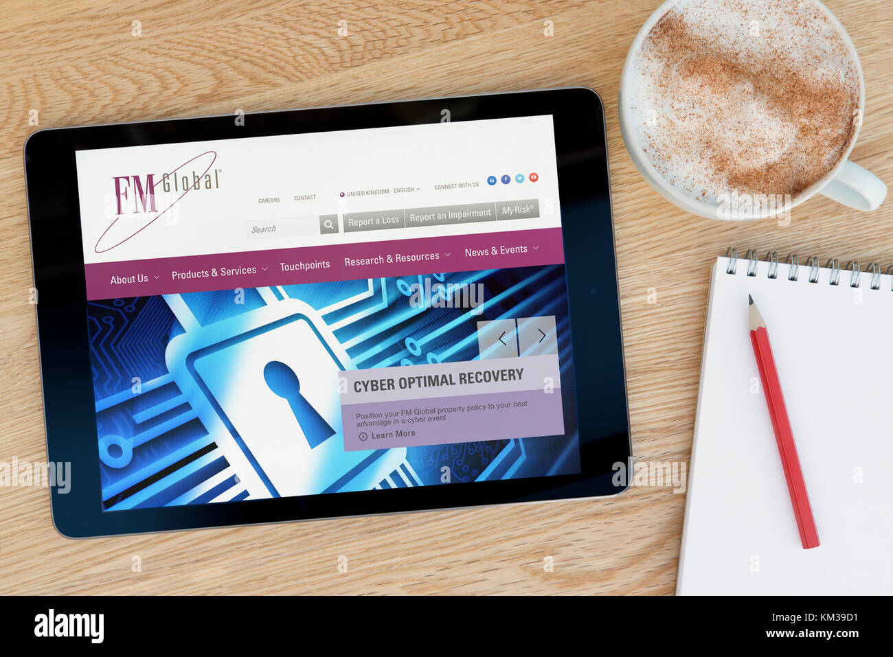 Le site web de l'assurance-FM Global sur un iPad tablet device qui repose sur une table en bois à côté d'un bloc-notes et un crayon et une tasse de café (rédaction uniquement) Banque D'Images