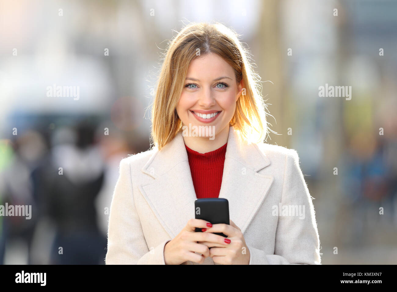 Vue avant portrait of a woman posing looking coat à vous tenir un téléphone intelligent dans la rue en hiver Banque D'Images