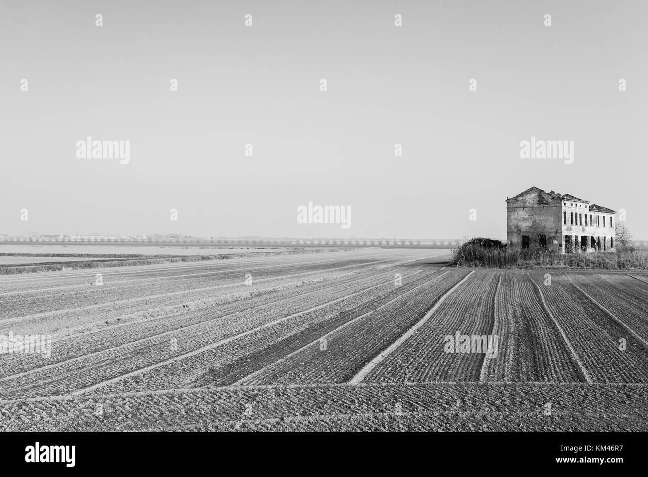 Paysage italien rurale à partir de la rivière Po lagoon.champs ensemencés avec des lignes de perspective. Entrepôt désaffecté. Modifié numériquement Image Banque D'Images