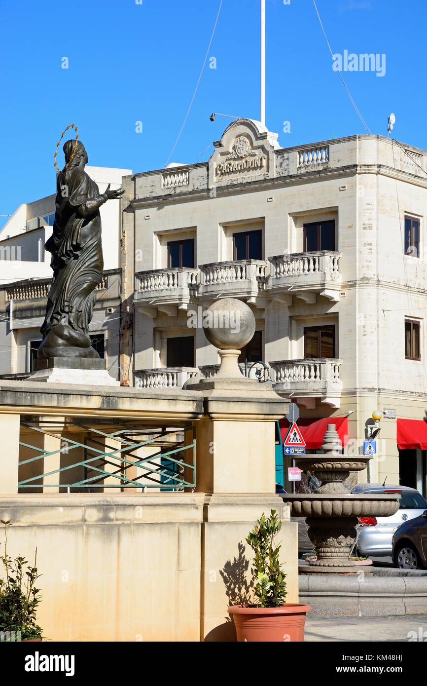 Statue devant le dôme de Mosta avec les entreprises et de l'ancien cinéma Paramount à l'arrière des bâtiments autour de la place de la rotonde dans le centre-ville, Mosta, Banque D'Images