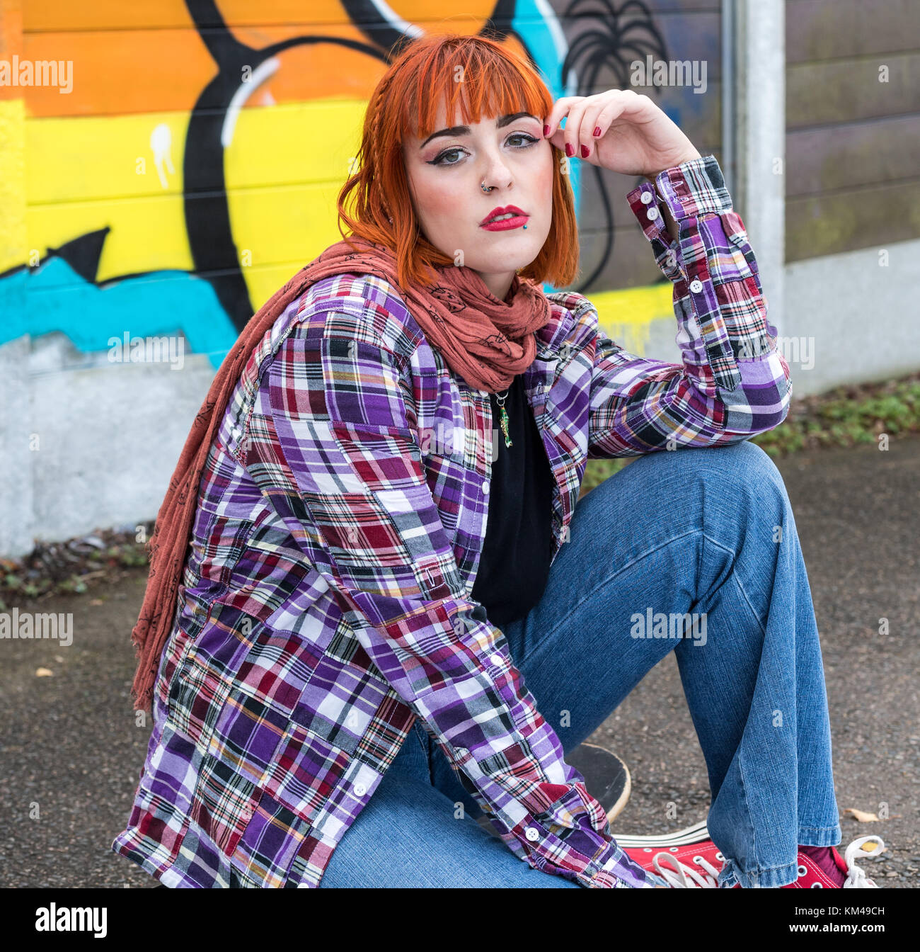 Jolie jeune femme portant des jeans et chemise à carreaux à la recherche dans l'appareil photo tout en étant assis. Banque D'Images