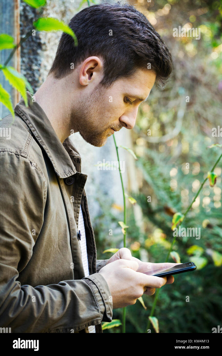 Un jeune homme en veste marron texto en utilisant un téléphone intelligent Banque D'Images