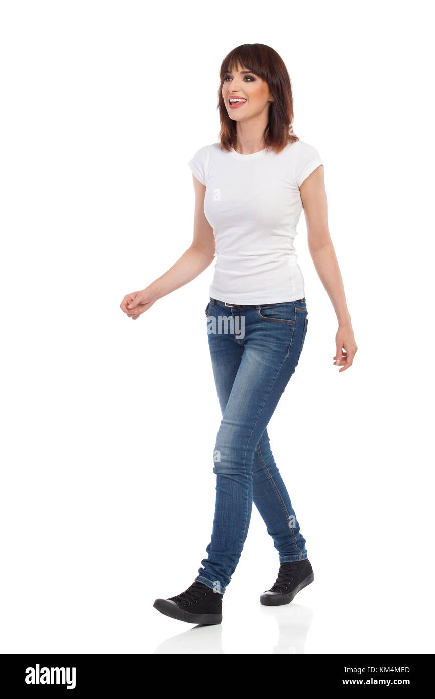 Jeune femme en jeans et t-shirt blanc est la marche, à l'écart et parler. full length portrait isolé sur blanc. Banque D'Images