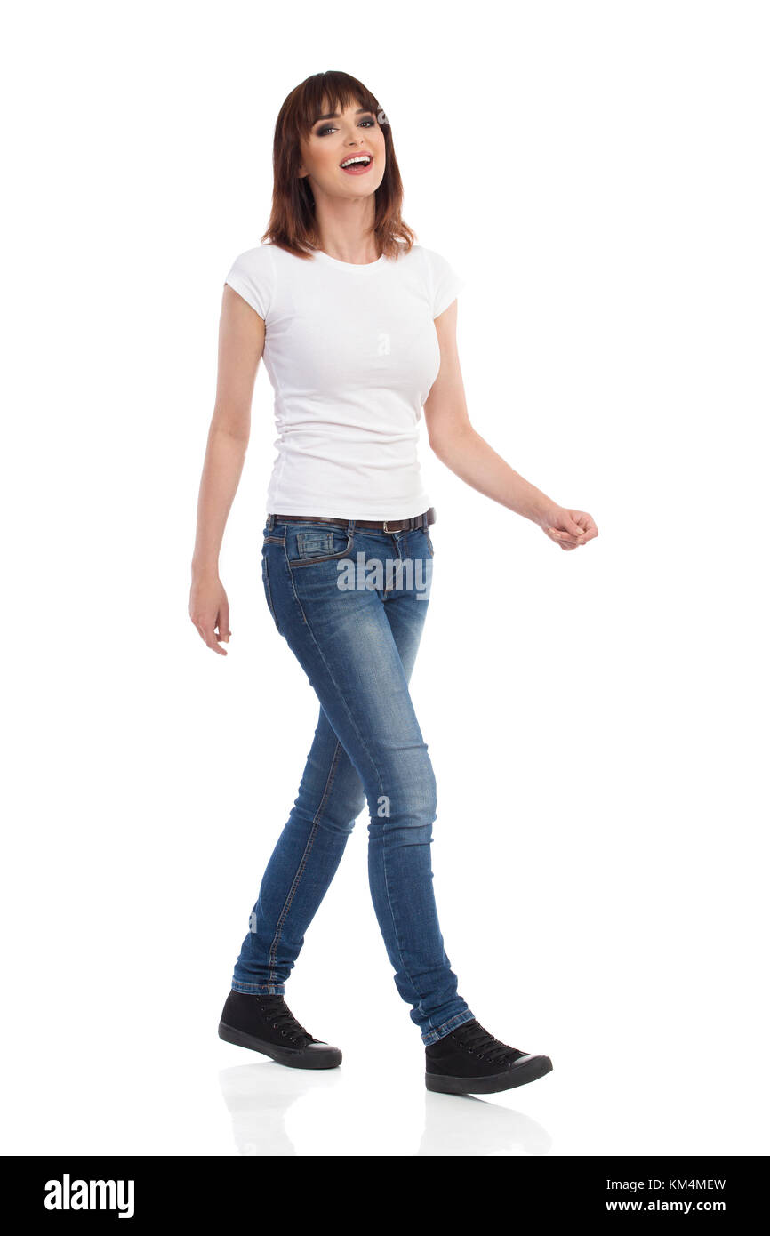 Jeune femme en jeans et t-shirt blanc est la marche, à la caméra et au rire. full length portrait isolé sur blanc. Banque D'Images