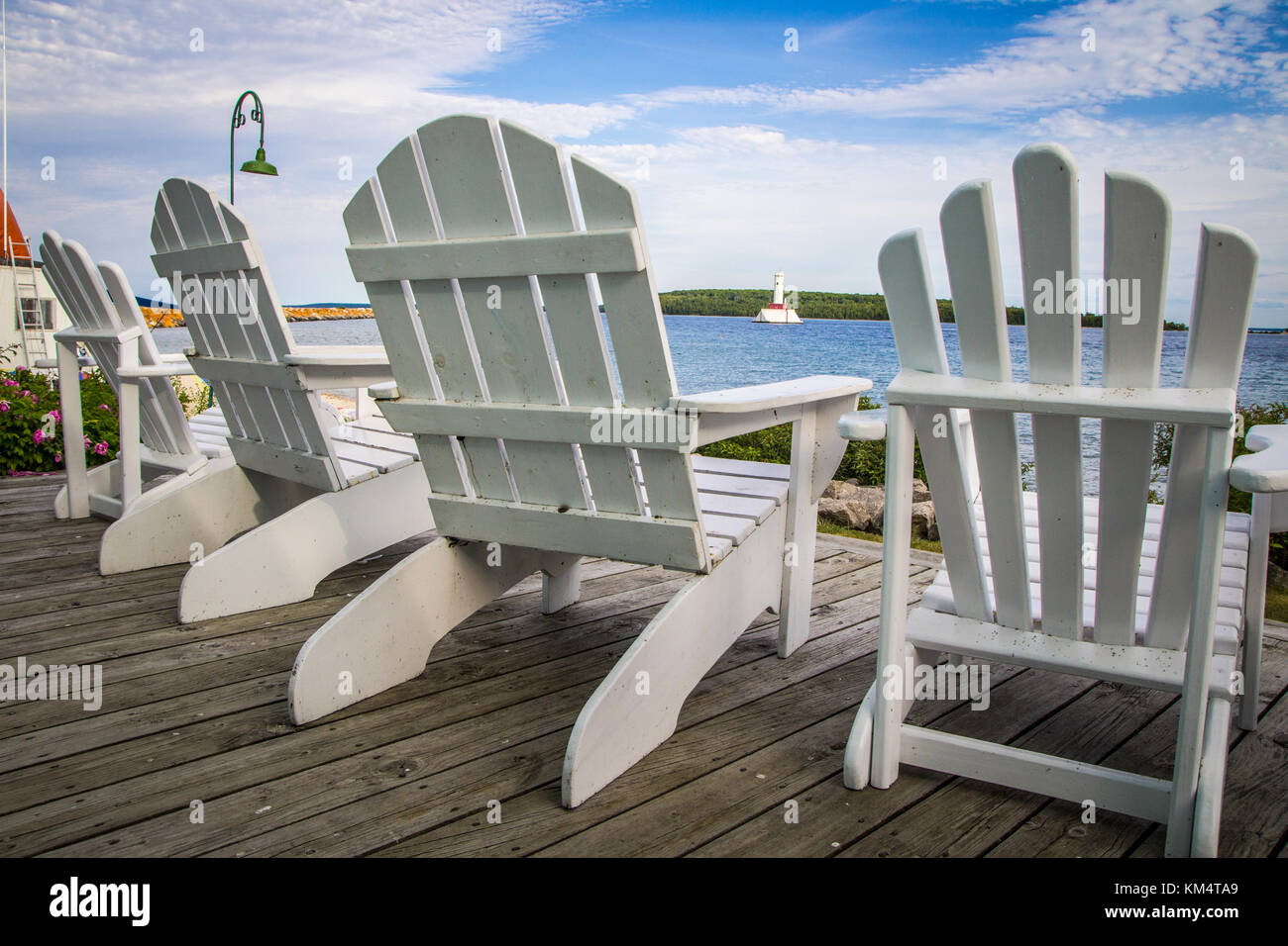 Style de vie côtière. Chaises Adirondack blanc sur un pont au bord de l'eau en bois avec une vue front de mer, et le phare. Mackinaw Island, Michigan, USA. Banque D'Images