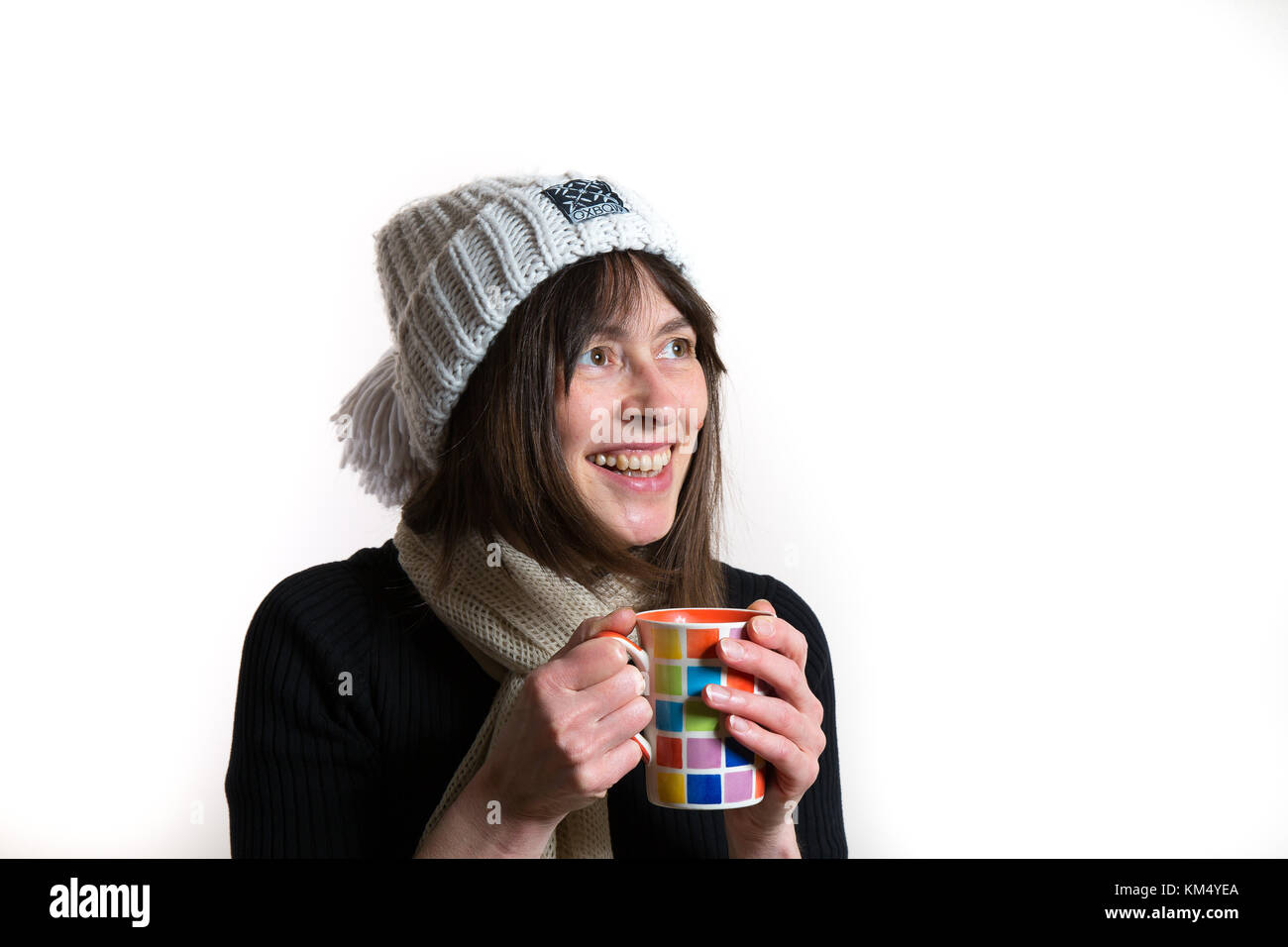 Portrait intérieur d'une heureuse femelle caucasienne isolée dans un chapeau de beanie bobble, chauffe les mains sur le mug. Beau grand sourire naturel. Banque D'Images