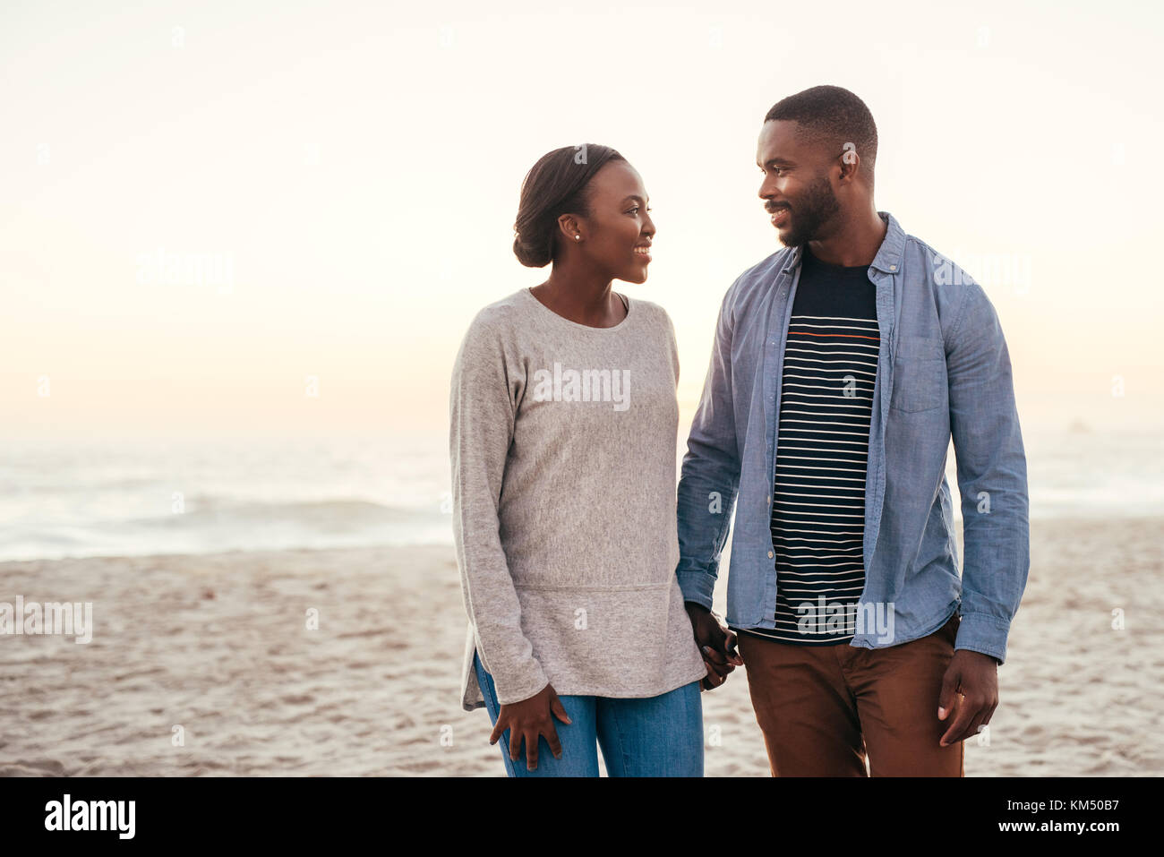 Smiling african couple en train de marcher ensemble le long d'une plage au coucher du soleil Banque D'Images