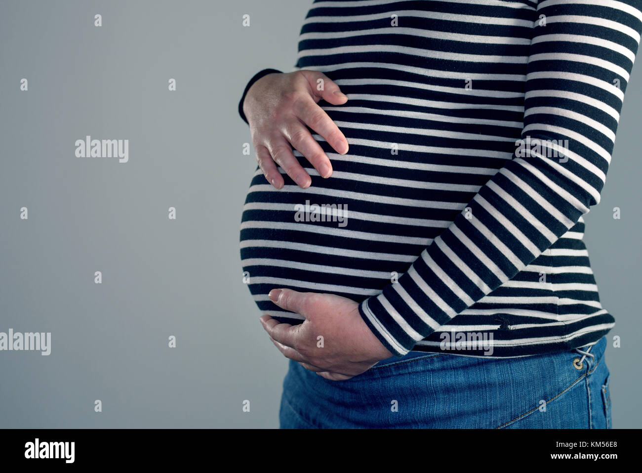 Close-up of pregnant woman with hands over ventre sur fond gris clair Banque D'Images