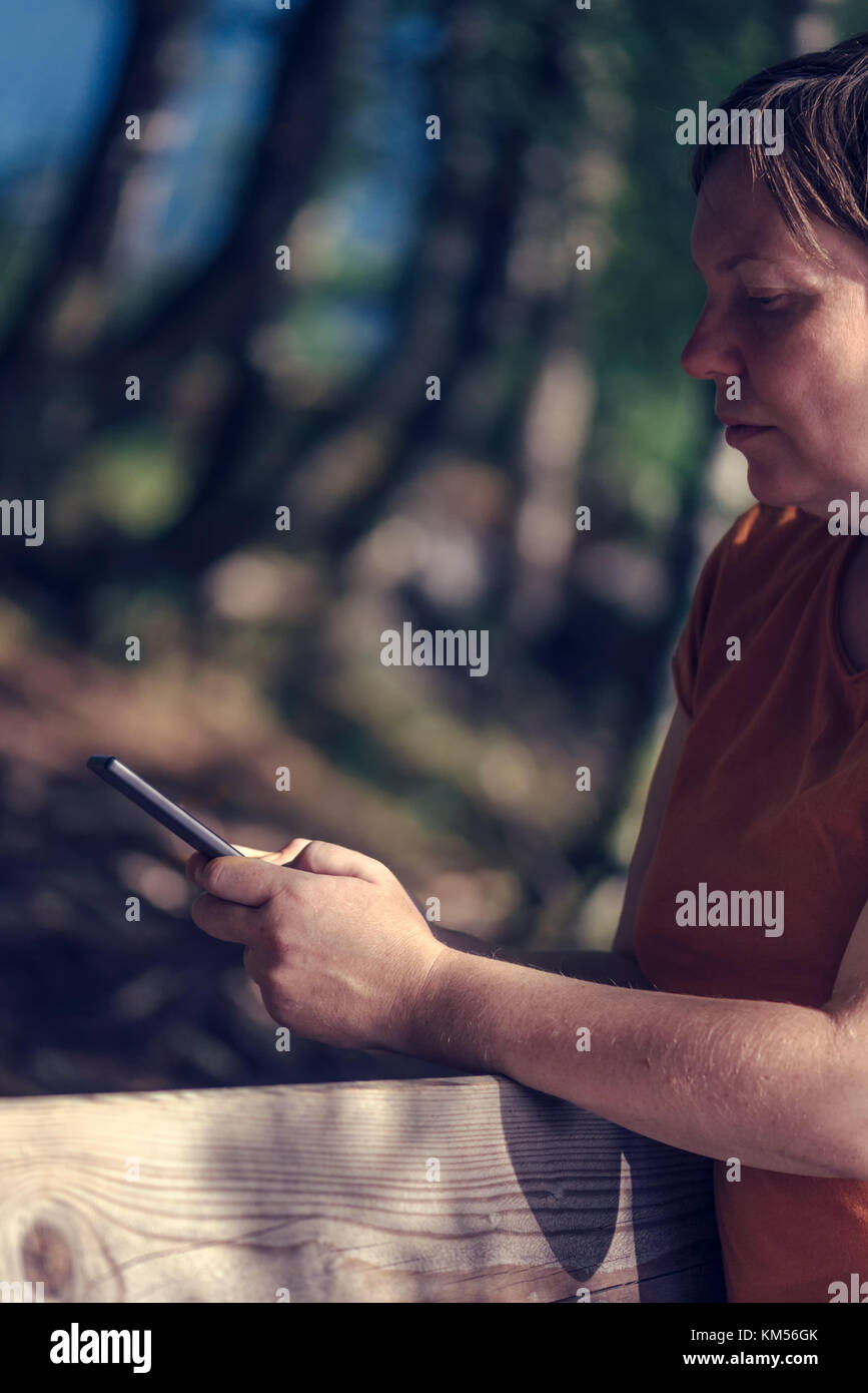 Pregnant woman texting outdoors on park bench, adulte femelle de race blanche à l'aide de téléphone mobile pendant la grossesse Banque D'Images