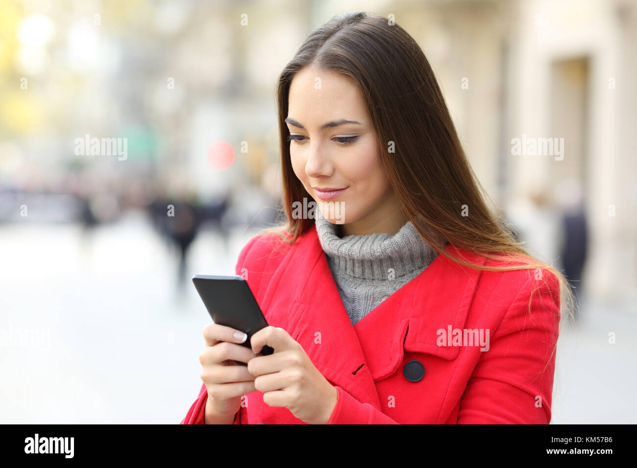 Femme sérieuse à l'aide d'un smart phone debout sur la rue en hiver Banque D'Images