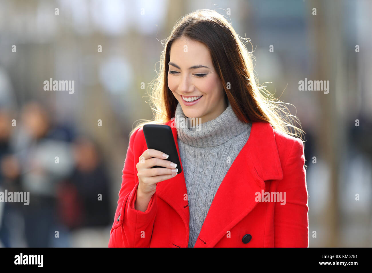 Heureux femme portant un manteau rouge et marche à l'aide d'un téléphone intelligent dans la rue en hiver Banque D'Images