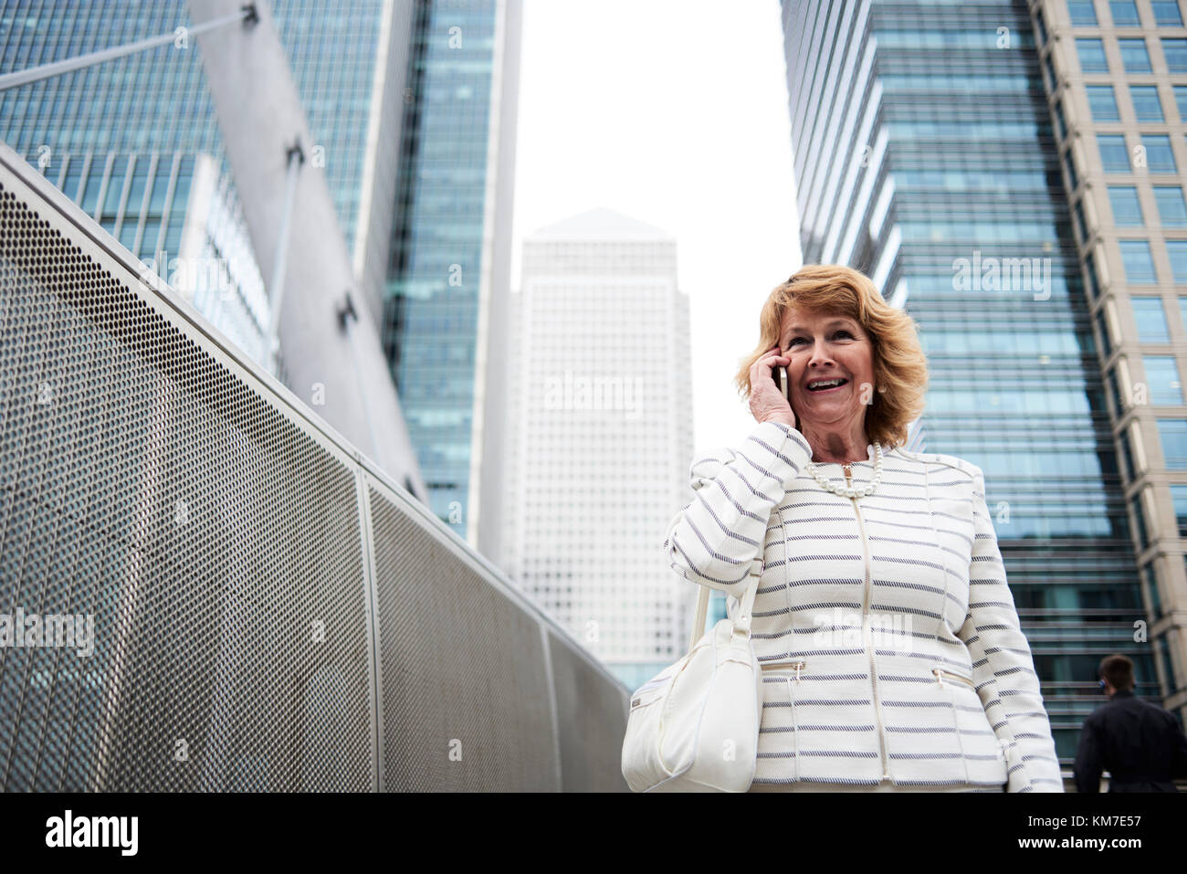 Londres, Royaume-Uni, jolie senior business woman chatting over le téléphone en souriant et entouré de bâtiments d'affaires, femmes d'affaires senior Banque D'Images