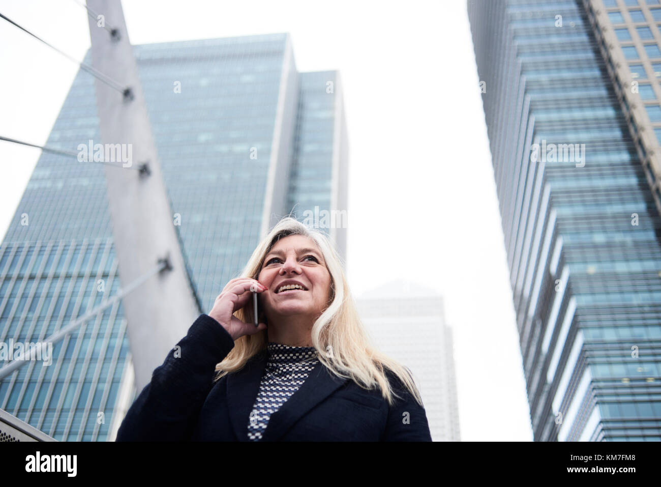 Londres, Royaume-Uni, jolie senior business woman chatting over le téléphone en souriant et entouré de bâtiments d'affaires, femmes d'affaires senior Banque D'Images