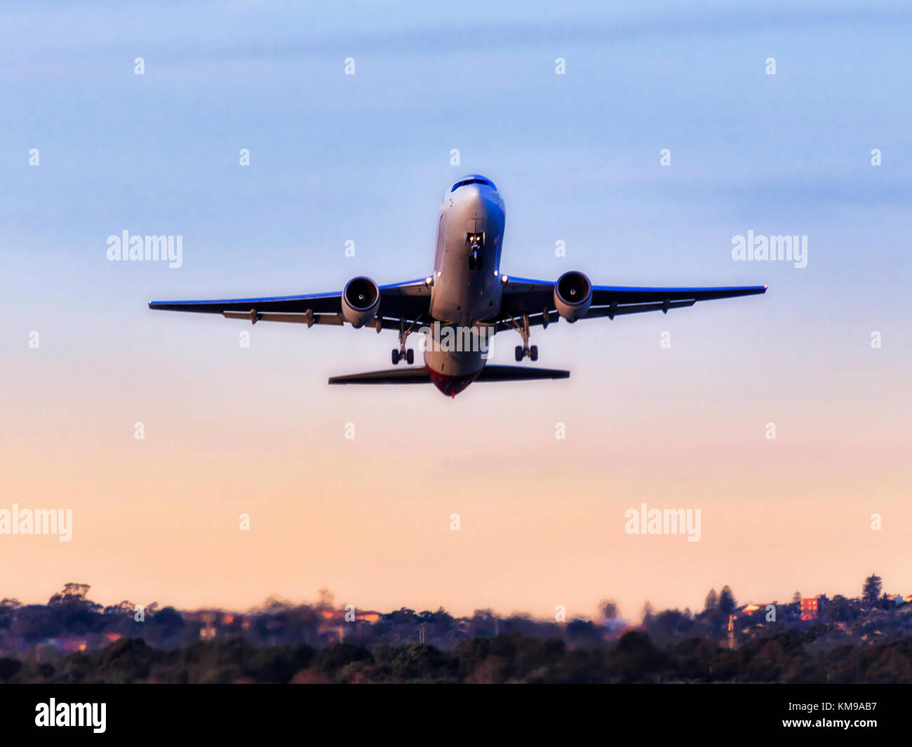 Passager moderne avion décollant de l'aéroport international de Sydney contre ciel bleu clair en vue de gommiers et banlieue résidentielle. Banque D'Images
