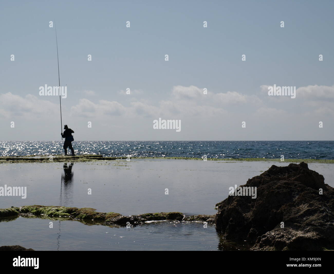 Debout sur la falaise, pêcheur avec sa canne à pêche sur le fond de l'horizon et le ciel bleu au-dessus Banque D'Images