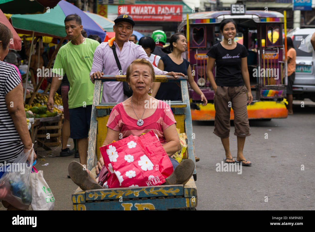 Une image humoristique d'une femme assise sur un chariot poussé par un homme à travers le marché du carbone, Cebu City Banque D'Images