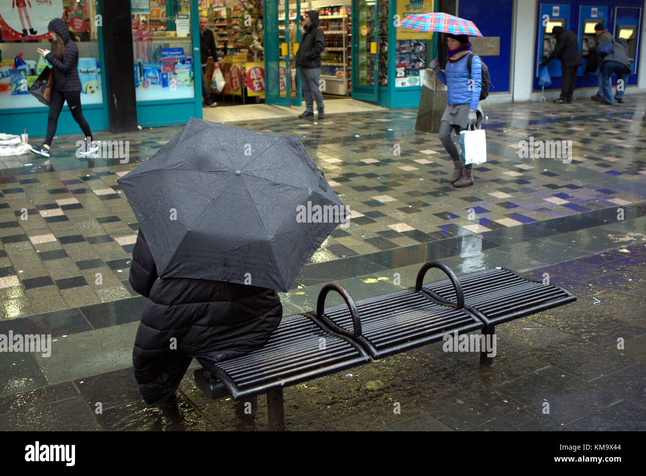 Fille avec parapluie noir assis sur le banc de la rue jour pluvieux humide Sauchiehall Street, Glasgow, Glasgow City, Royaume-Uni Banque D'Images