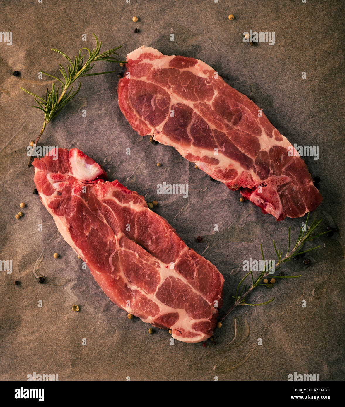Photo verticale de deux tranches de steaks de cou de porc. Les portions de viande par la couleur rouge et la graisse est placée sur la plaque à pâtisserie de papier usé avec poivre, rosema Banque D'Images
