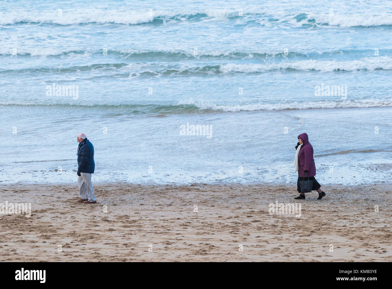 Un homme marchant le long de Fistral Beach avec sa femme suivant derrière à Newquay Cornwall Royaume-Uni. Banque D'Images