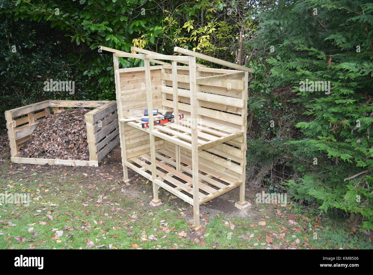 Journal bois store en cours de construction dans le jardin avec du compost heap fait de re-palettes pleine de feuilles et l'herbe coupée montrant également vers la gauche Banque D'Images