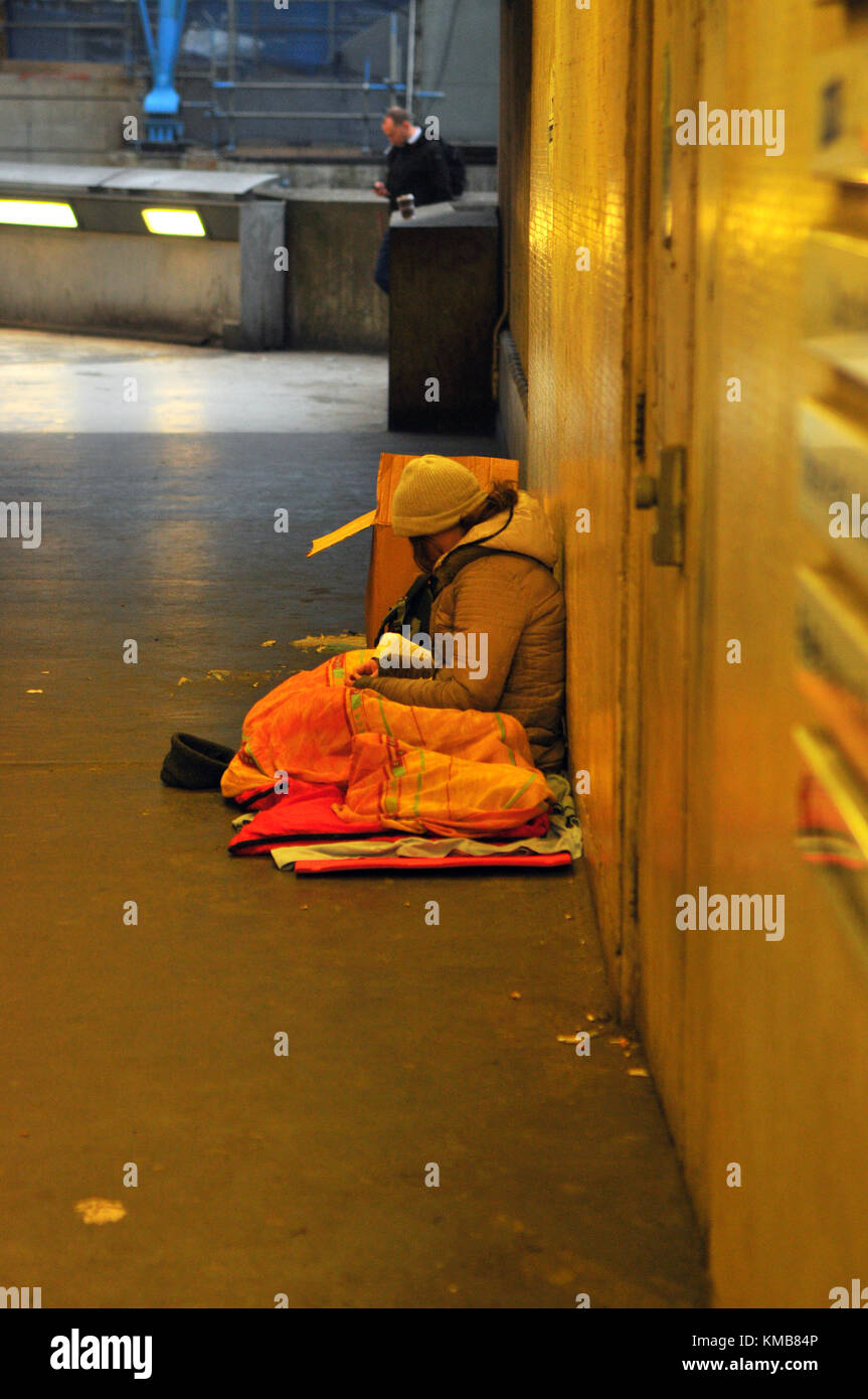 Une personne sans-abri dorment dans la rue sous le carton à la gare de Waterloo à Londres recouvert d'une couverture en lambeaux et assis avec les jambes croisées pour garder au chaud Banque D'Images