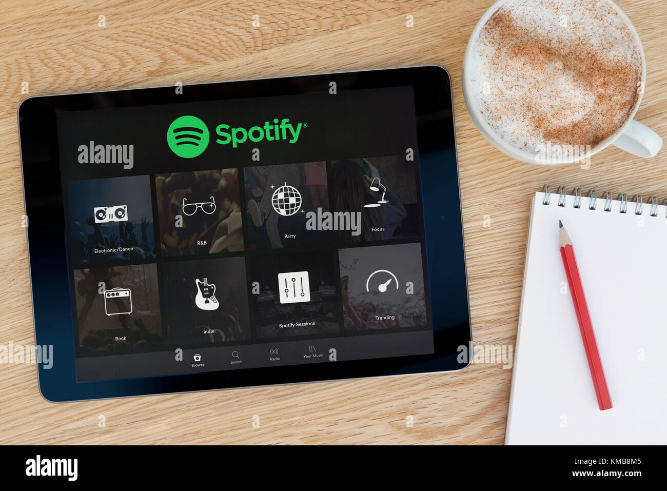 L'application Spotify dispose sur un iPad tablet device qui repose sur une table en bois à côté d'un bloc-notes et un crayon et une tasse de café (rédaction uniquement) Banque D'Images