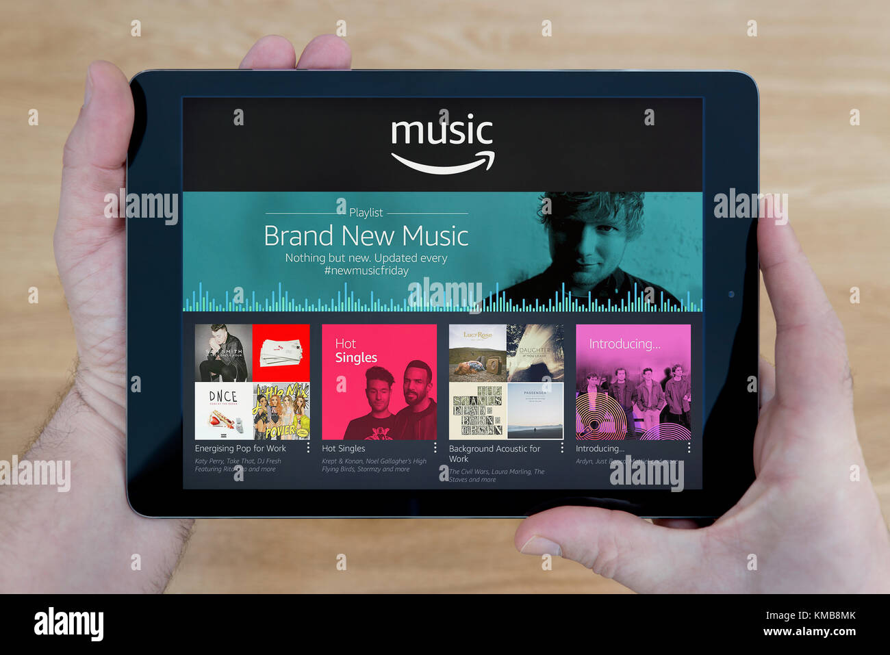 Un homme regarde l'Amazon Music site sur son iPad tablet device, tourné contre une table en bois page contexte (usage éditorial uniquement) Banque D'Images