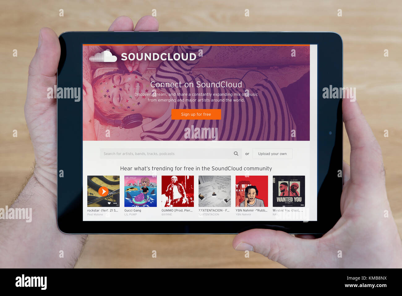 Un homme regarde le Soundcloud site sur son iPad tablet device, tourné contre une table en bois page contexte (usage éditorial uniquement) Banque D'Images