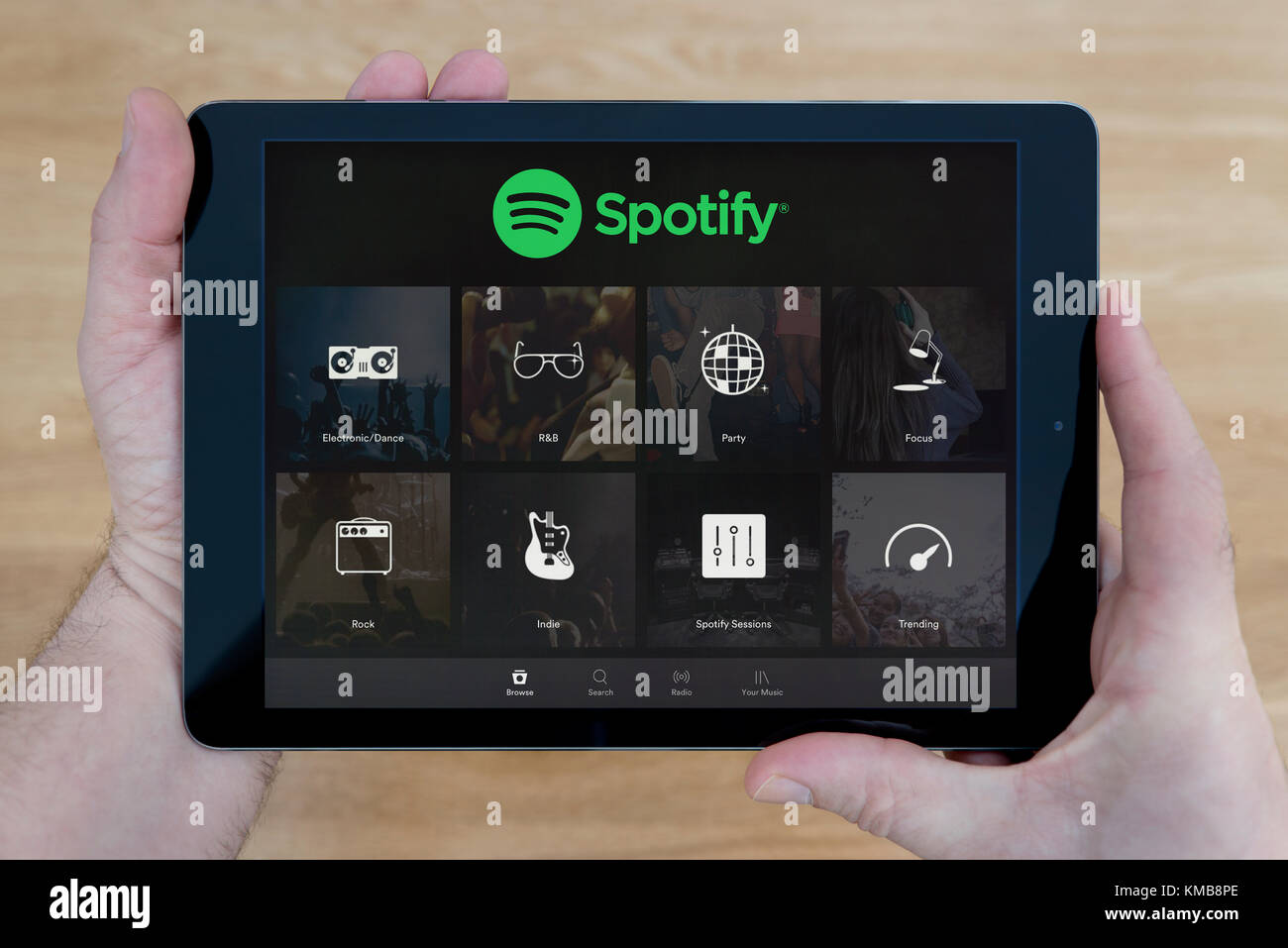 Un homme regarde l'application Spotify sur son iPad tablet device, tourné contre une table en bois page contexte (usage éditorial uniquement) Banque D'Images