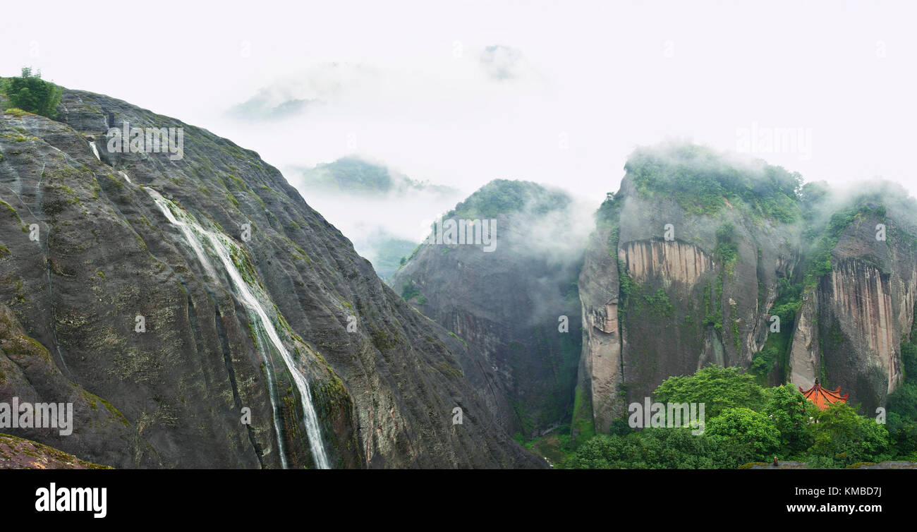 Vue panoramique de belles montagnes couvertes de brouillard magique avec petite chute d'eau et pagode asiatique montrant entre arbres dans wuyishan mountains national p Banque D'Images