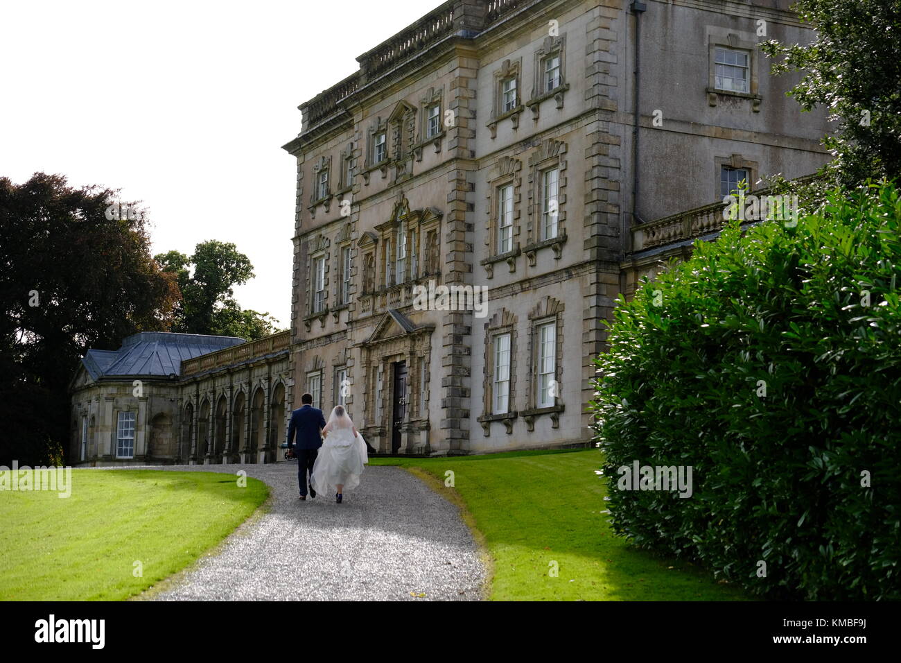 Wedding couple marchant vers une amende Manor House en Irlande du Nord. l'homme a un costume bleu et chaussures brunes et la dame est dans un mariage merveilleux Banque D'Images