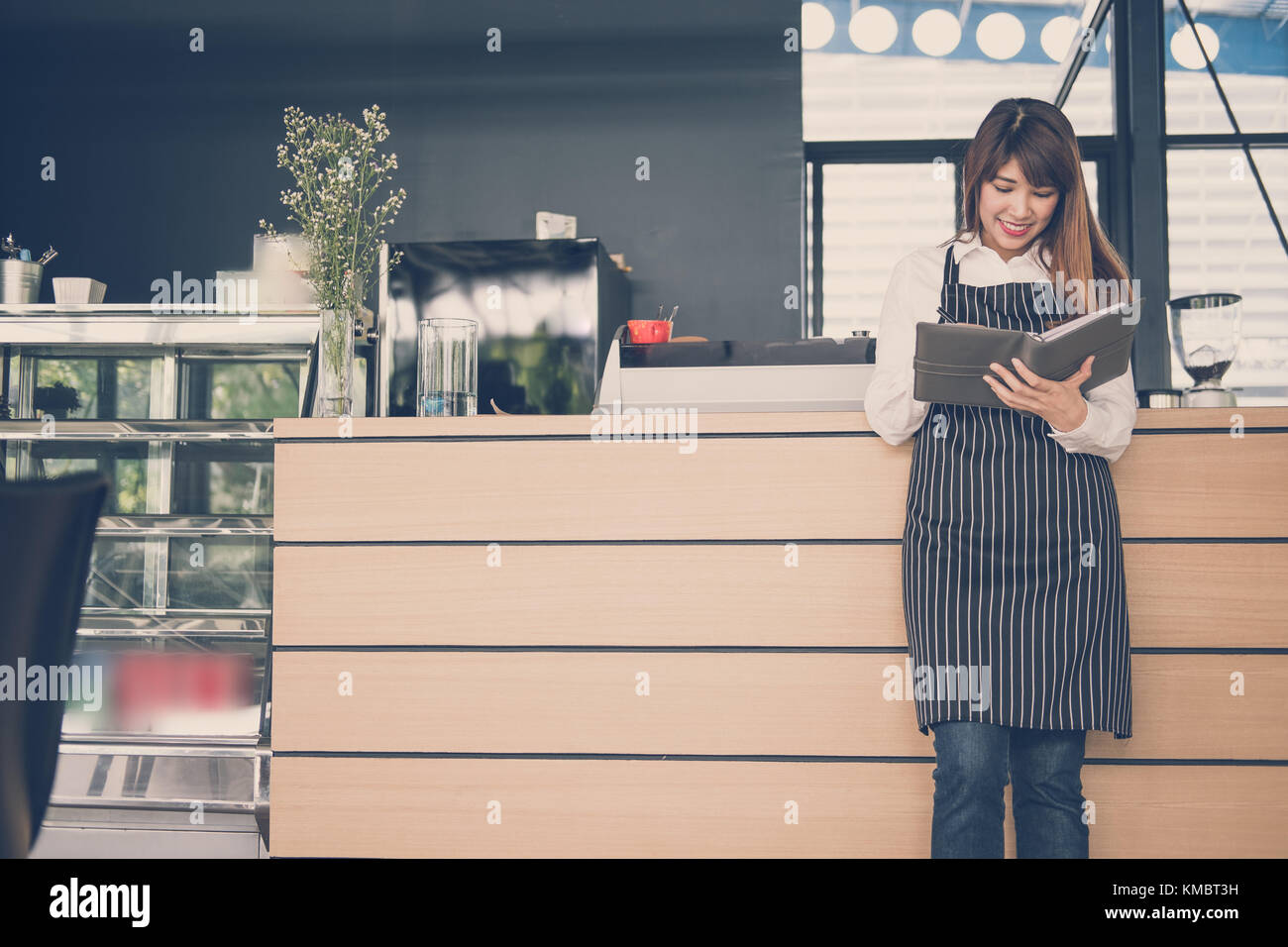Propriétaire de petite entreprise holding notebook au comptoir à café. asian female barista portant un tablier écrit la note à la bar dans le café. Les services alimentaires, restaur Banque D'Images