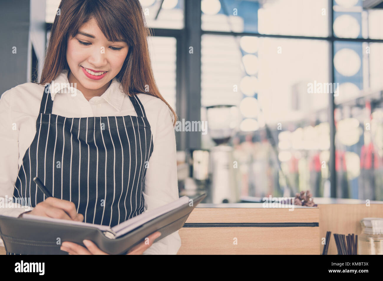 Propriétaire de petite entreprise holding notebook au comptoir à café. asian female barista portant un tablier écrit la note à la bar dans le café. Les services alimentaires, restaur Banque D'Images