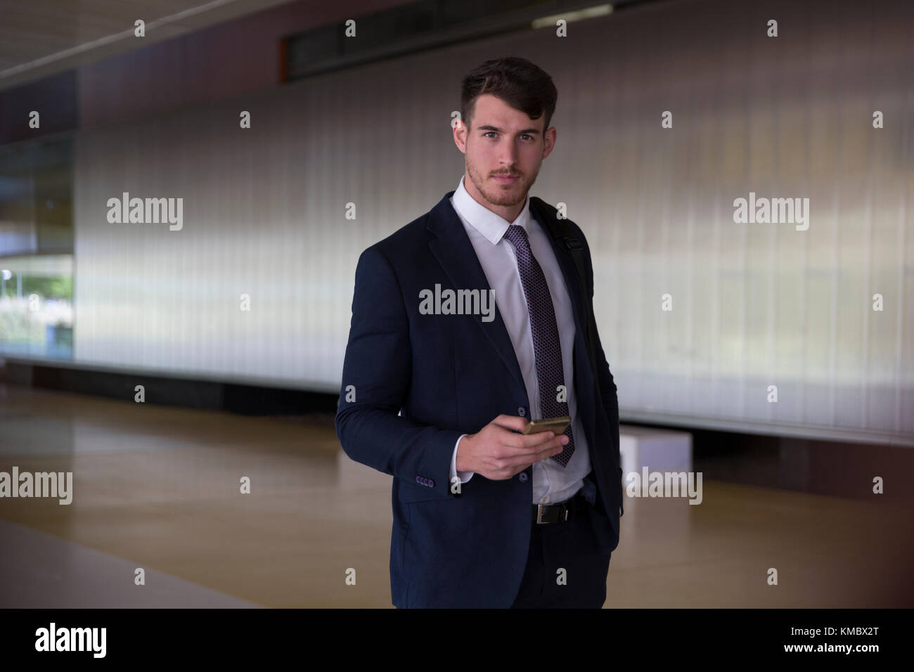 Portrait confiant, homme d'affaires sérieux textant avec un smartphone dans le hall du bureau Banque D'Images