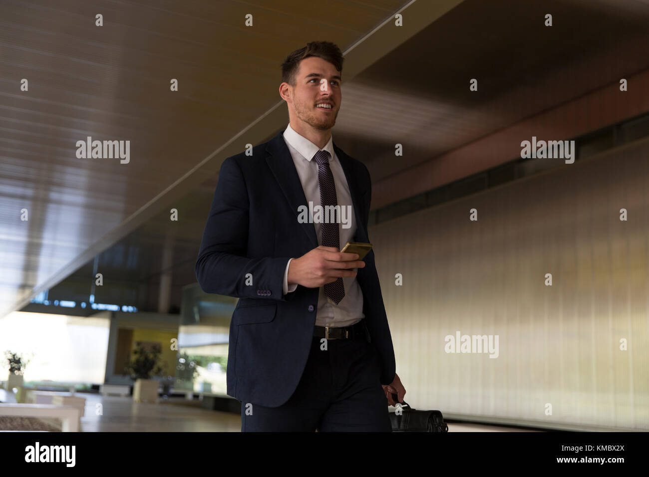 Homme d'affaires marchant avec un smartphone dans le hall du bureau Banque D'Images