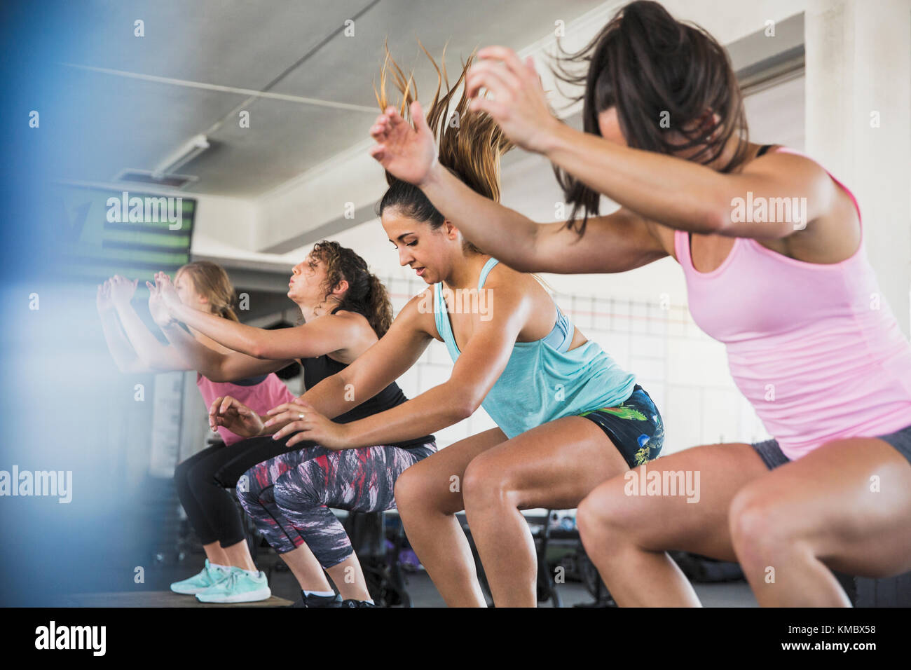 Jeunes femmes qui font des squats de saut en classe d'exercice Banque D'Images