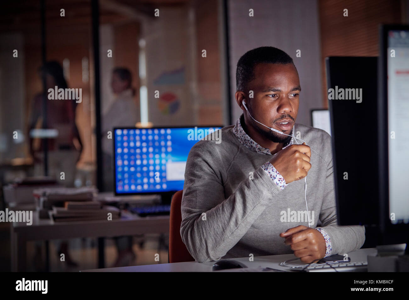 Homme d'affaires travaillant tard à l'ordinateur, en utilisant des écouteurs mains libres parlant au téléphone Banque D'Images