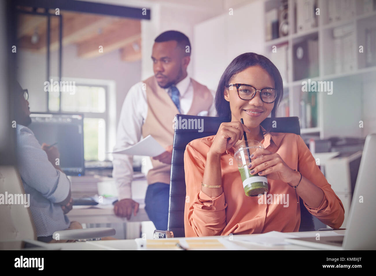 Portrait smiling confident businesswoman drinking smoothie vert in office Banque D'Images