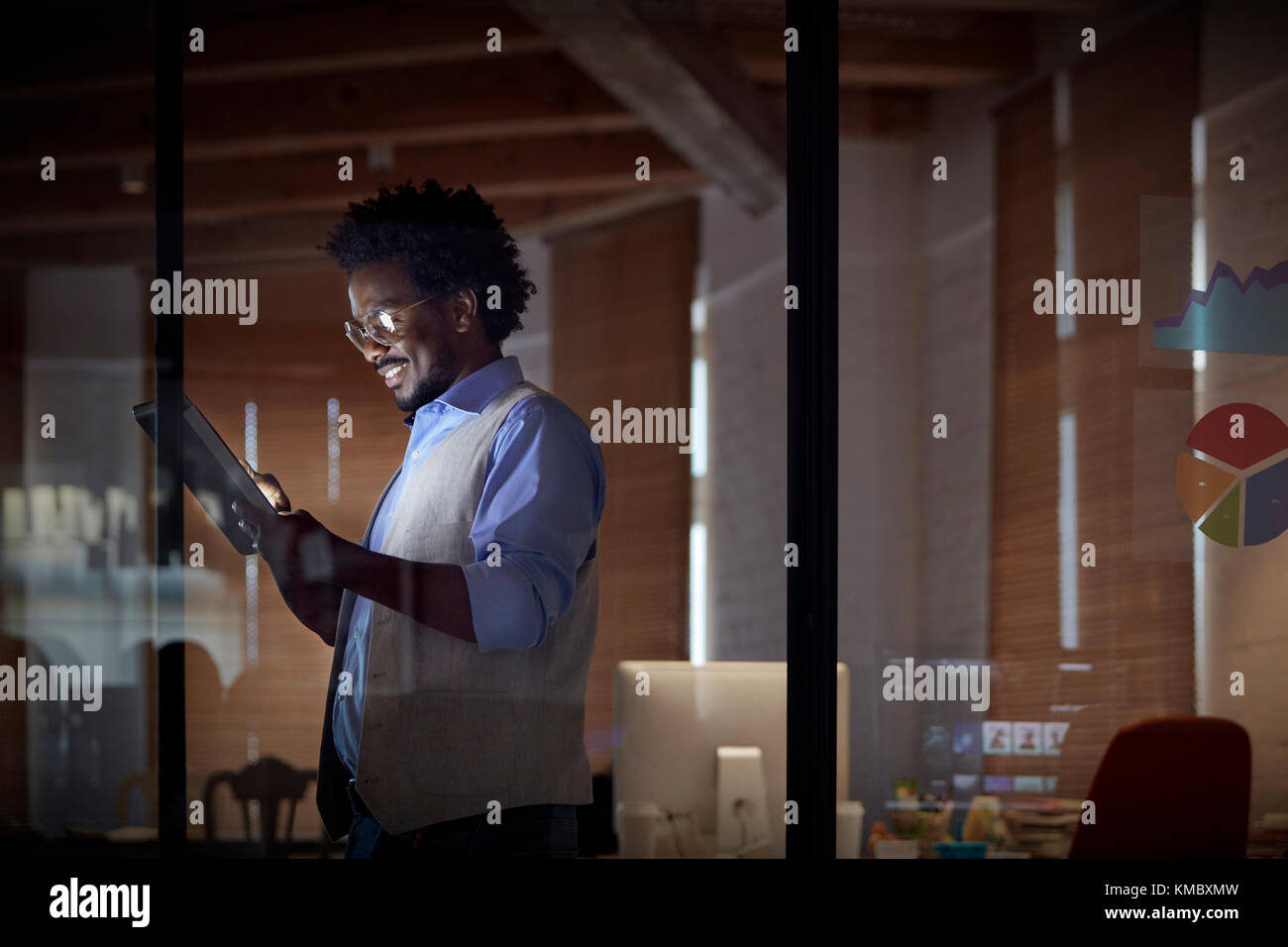 Femme d'affaires souriante travaillant tard, utilisant une tablette numérique dans le bureau sombre à nuit Banque D'Images