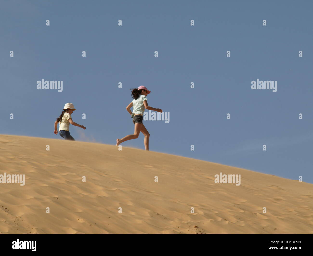 2 filles s'exécutant sur une dune de sable sur le fond de ciel Banque D'Images