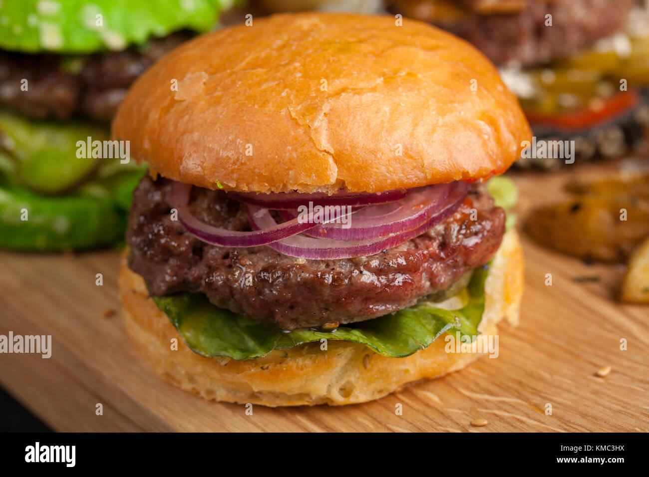 Gros plan d'un ensemble de trois mini-hamburgers faits maison avec du bœuf en marbre et des légumes sur une planche en bois. Banque D'Images