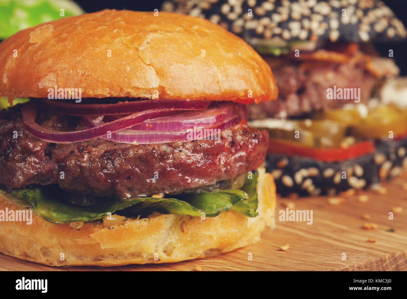 Gros plan d'un ensemble de trois mini-hamburgers faits maison avec du bœuf en marbre et des légumes sur une planche en bois. Banque D'Images