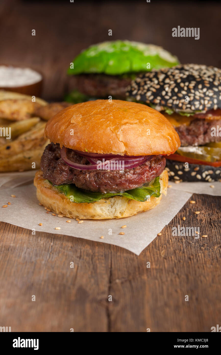 Gros plan d'un ensemble de trois mini-hamburgers faits maison avec du bœuf en marbre et des légumes sur une planche en bois. Banque D'Images