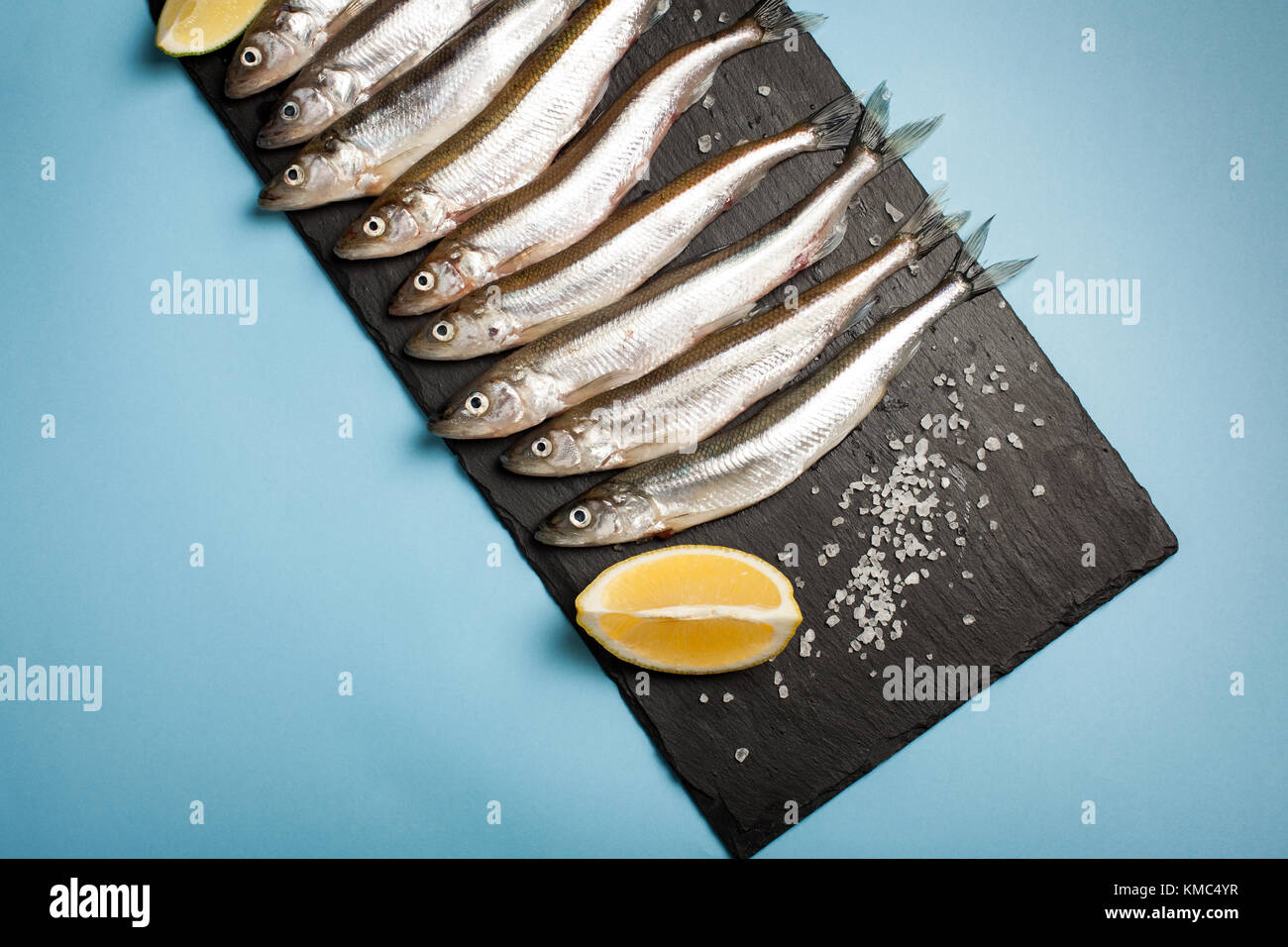 Poisson frais de la mer ou l'éperlan et prête pour la cuisson des sardines au citron, thym, gros sel de mer et sur un fond bleu. Le concept de frais, sain de fruits de mer. Vue de dessus Banque D'Images