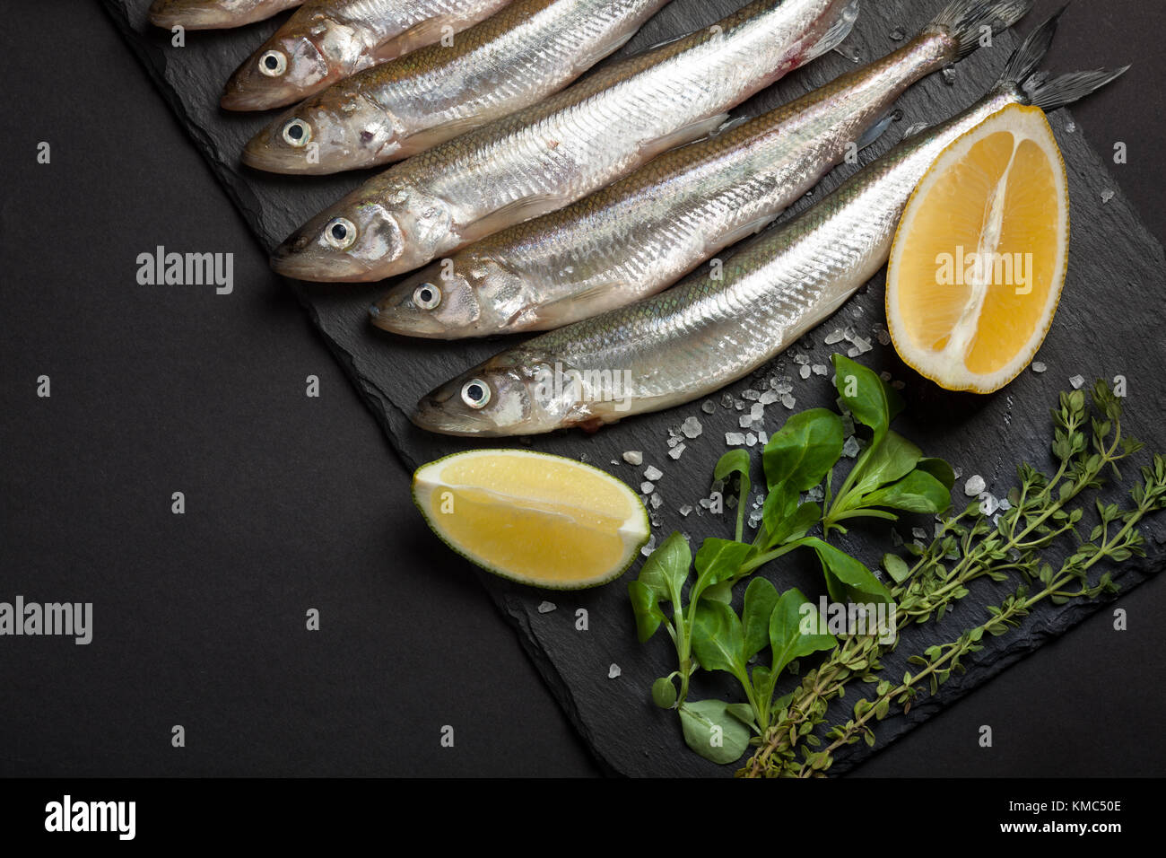 Poisson frais de la mer ou l'éperlan et prête pour la cuisson des sardines au citron, thym, gros sel de mer et sur un fond noir. Le concept de frais, sain de fruits de mer. Vue de dessus Banque D'Images